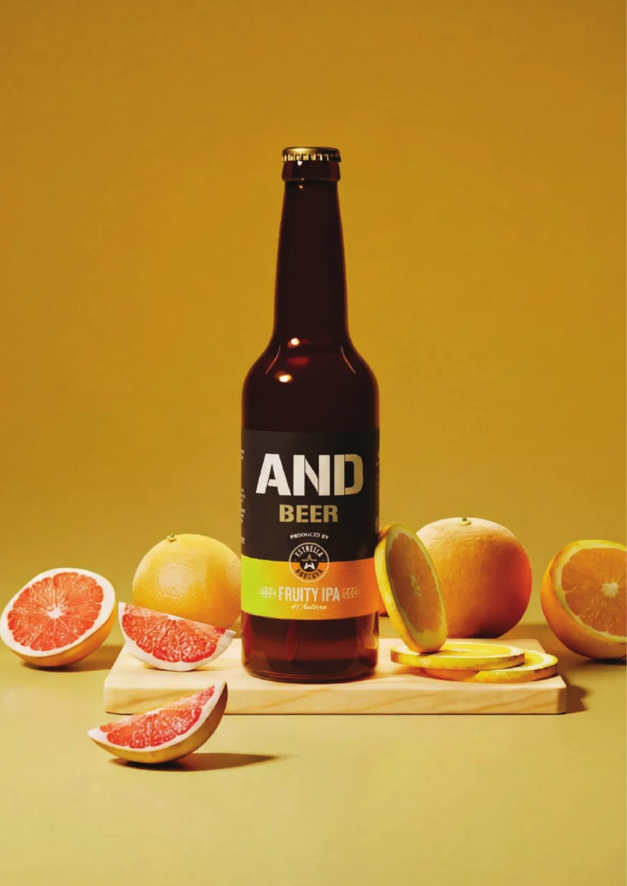 Ampolla de Fruity IPA d'Estrella Andorra amb cítrics tallats sobre fons mostassa
